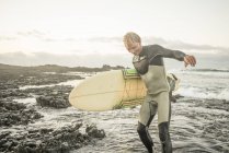 Людина в гідрокостюмі і тримає дошку для серфінгу — стокове фото