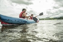 Hombre y niño en kayak remando lejos de la orilla - foto de stock