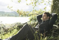 Чоловік розслабляється проти дерева на березі — стокове фото