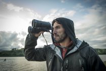 Man using binoculars on shore — Stock Photo