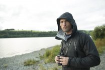 Uomo in piedi con binocolo sulla riva — Foto stock