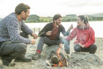 Tre amici che arrostiscono marshmallow sulla riva — Foto stock