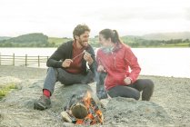 Couple relaxing around campfire on shore — Stock Photo