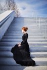 Woman sitting on steps in black gown — Stock Photo