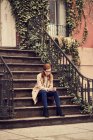 Женщина сидит на ступеньках на смартфоне — стоковое фото