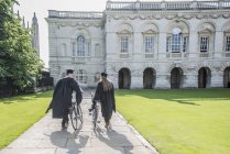 Студенти у випускних сукнях штовхають велосипеди — стокове фото