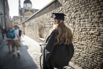 Student in graduation gown cycling along passageway — Stock Photo