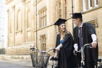 Young students in graduation gowns cycling — Stock Photo