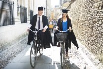 Молоді студенти у випускних сукнях їзда на велосипеді — стокове фото