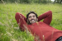 Homme en pull rouge relaxant dans l'herbe — Photo de stock