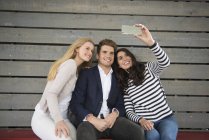 Friends sitting on bench taking selfie — Stock Photo