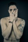 Uomo tatuato che copre il viso con le mani — Foto stock