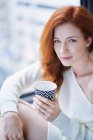 Woman with hot drink sitting by window — Stock Photo