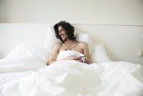Мужчина с длинными волосами лежит в постели с чашкой чая — стоковое фото
