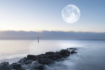 Paisagem sobre rochas no mar com lua gigante — Fotografia de Stock