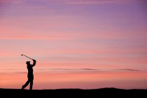 Man playing golf on colourful sunset — Stock Photo