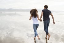 Пара бігає, тримаючись за руки на пляжі — стокове фото