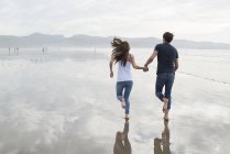 Casal correndo enquanto de mãos dadas na praia — Fotografia de Stock