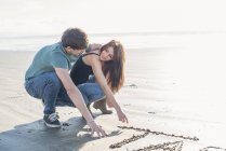 Couple drawing in sand on beach — Stock Photo