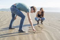 Paar zeichnet im Sand am Strand — Stockfoto