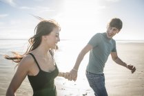 Пара бежит, держа руки на пляже — стоковое фото
