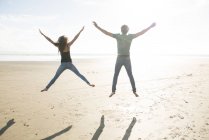 Casal pulando na luz do sol na praia — Fotografia de Stock