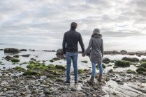 Пара стоїть, тримаючись за руки на пляжі — стокове фото