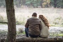 Couple sitting on log in forest — Stock Photo