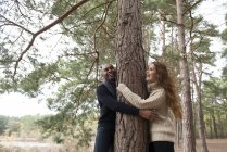 Pareja abrazando árbol durante paseo por el bosque - foto de stock