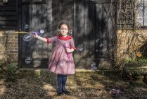 Chica soplando burbujas por puerta de garaje - foto de stock