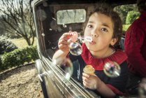 Menina soprando bolhas para fora da janela — Fotografia de Stock