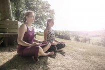 Friends sit at meadow and practice yoga — Stock Photo