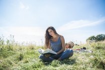 Женщина читает книгу, сидя на лугу — стоковое фото