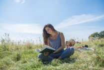 Frau liest Buch, während sie auf Wiese sitzt — Stockfoto