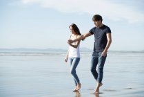 Пара ходьби, тримаючись за руки по пляжу — стокове фото