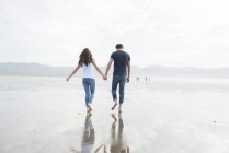 Coppia camminare tenendosi per mano attraverso la spiaggia — Foto stock