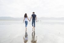 Пара ходить держась за руки через пляж — стоковое фото