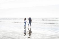 Пара ходить держась за руки через пляж — стоковое фото