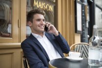 Людина сидить за межами кафе на телефон — стокове фото