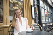 Жінка сидить за межами кафе розмовляє по телефону — стокове фото