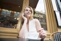 Femme assise devant un café parlant au téléphone — Photo de stock