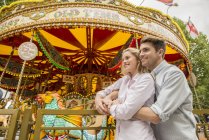 Couple cuddling in front of carousel — Stock Photo