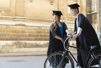 Estudantes em vestidos de graduação de ciclismo através de motivos — Fotografia de Stock