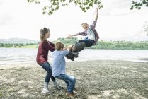 Девочка и мальчики играют на висящей на дереве шине — стоковое фото