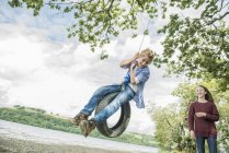 Mädchen und Junge spielen auf Reifen, die an Baum hängen — Stockfoto