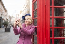 Frau macht Selfie vor einem Telefonkiosk — Stockfoto