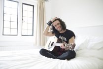 Молодий чоловік сидить на ліжку з гітарою — стокове фото
