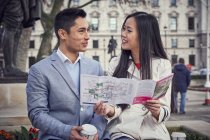 Couple sitting outside holding city guide — Stock Photo