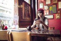 Frau sitzt am Tisch und nutzt Smartphone — Stockfoto