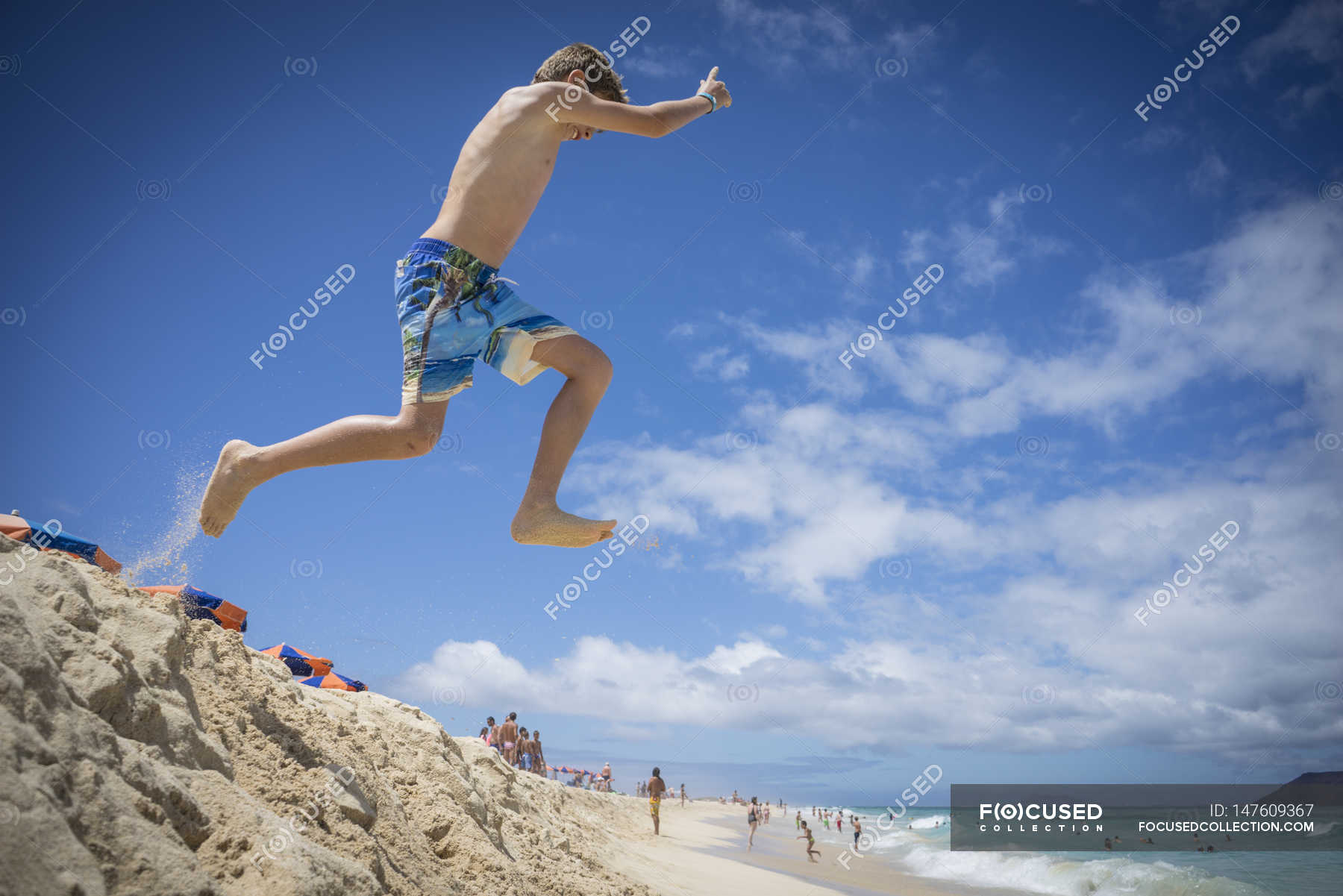 Boy jumping in sand dunes at beach — having fun, playing Stock Photo